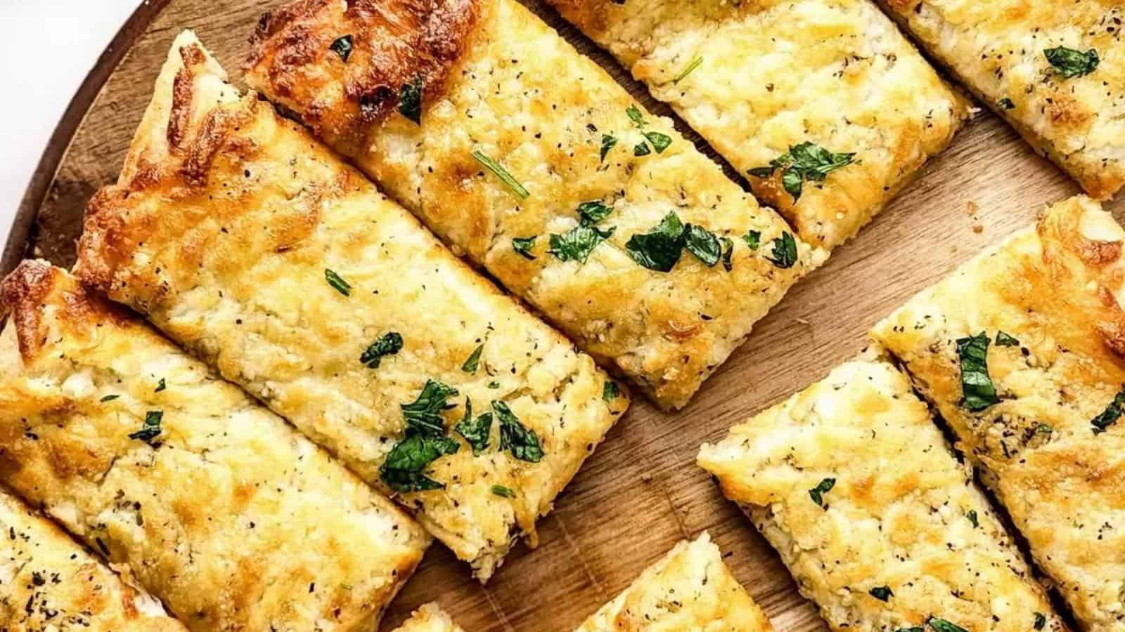 Slices of cheesy garlic bread topped with herbs, arranged on a wooden cutting board.
