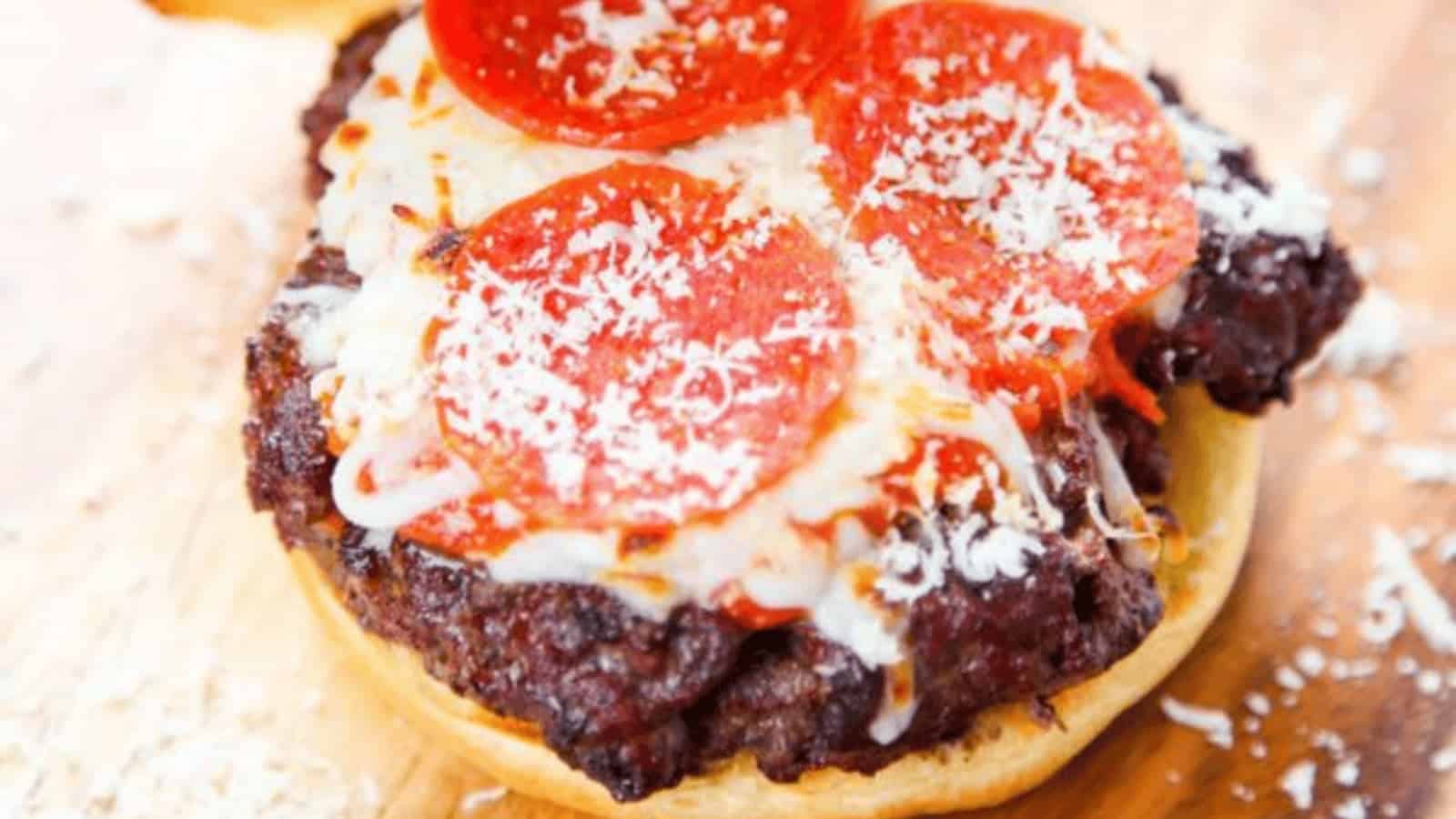 Open-faced burger topped with melted cheese, pepperoni slices, and grated cheese on a wooden surface.