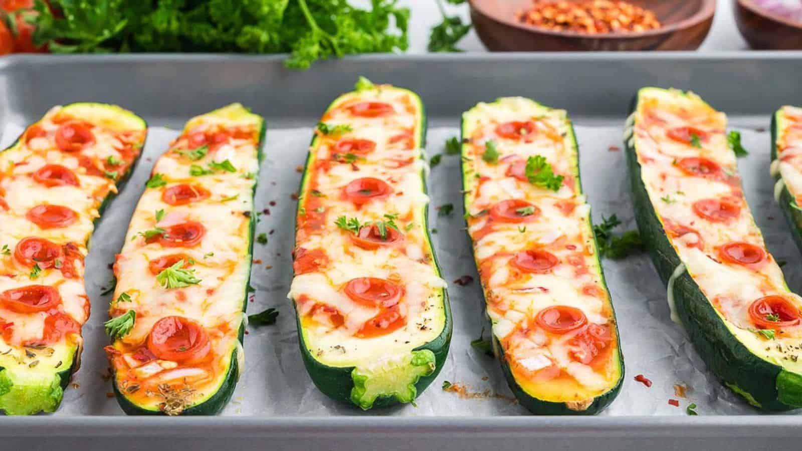 Baked zucchini halves topped with melted cheese, tomato slices, and herbs on a baking tray.