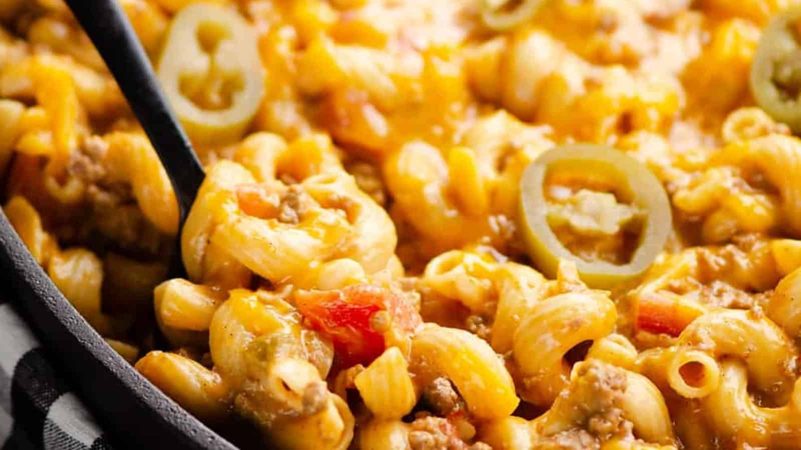 Close-up of cheesy macaroni with ground meat, diced tomatoes, and sliced jalape&ntilde;os in a skillet.