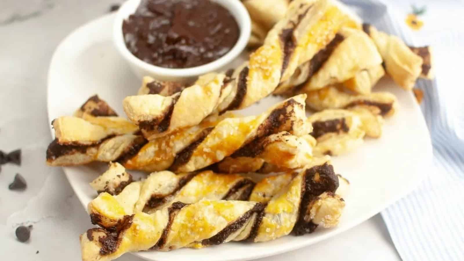 A plate of chocolate puff pastry twists with a small bowl of chocolate dipping sauce.