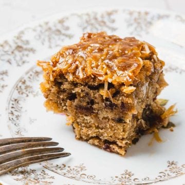 A square piece of German chocolate cake with coconut topping on a decorative plate next to a fork.