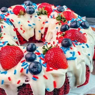 Bundt cake topped with white icing, strawberries, blueberries, and red, white, and blue sprinkles.
