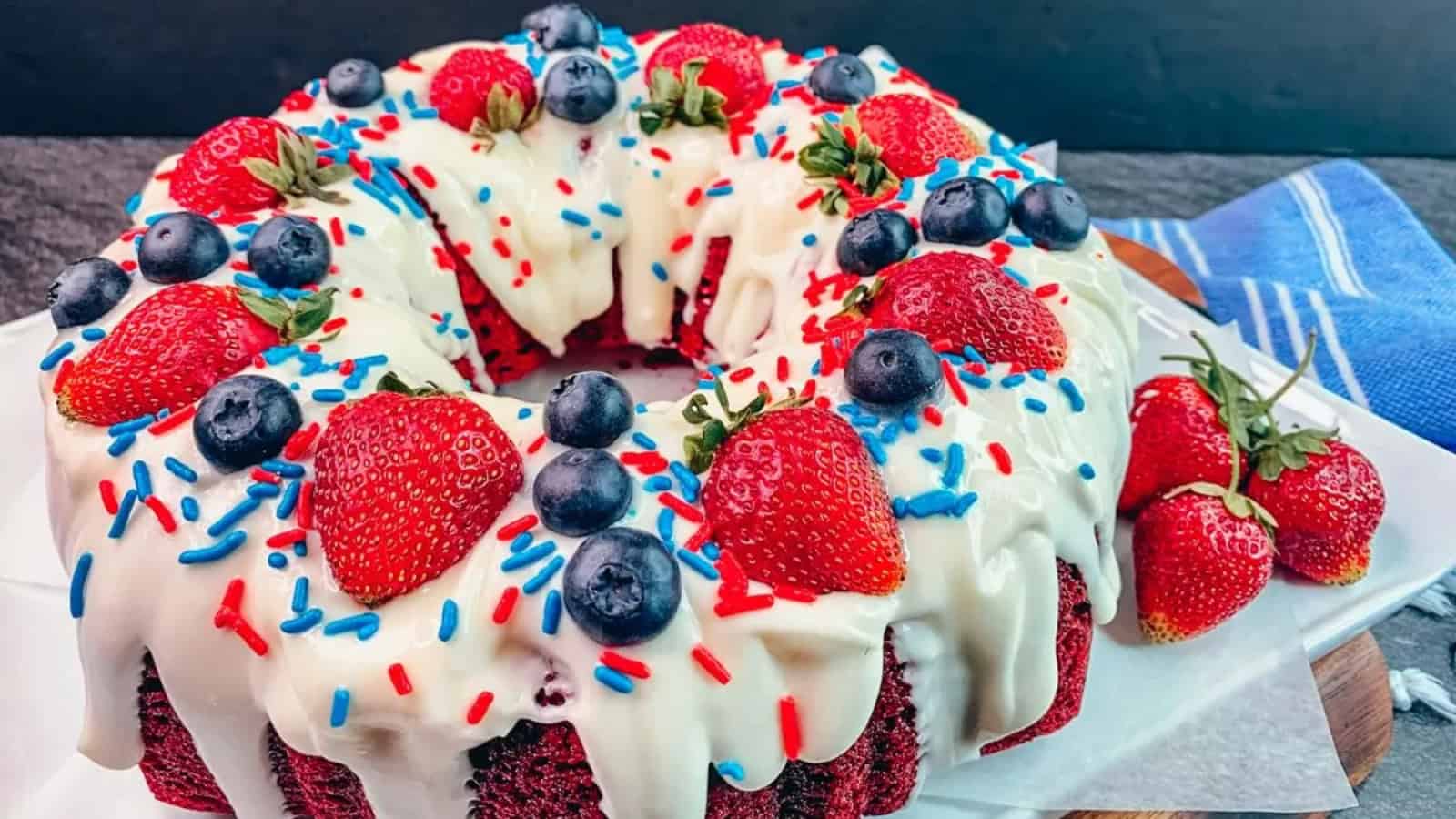 Bundt cake topped with white icing, strawberries, blueberries, and red, white, and blue sprinkles.