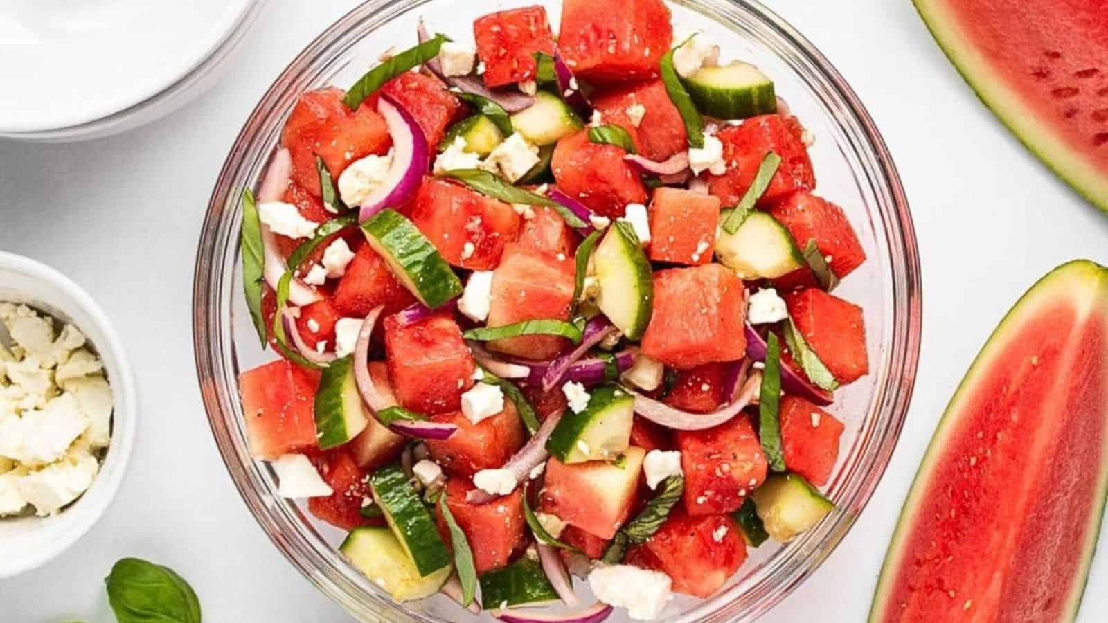 Bowl of watermelon salad with cucumber, red onion, feta cheese, and basil, viewed from above.