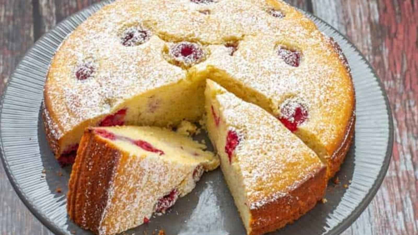 Round raspberry cake topped with powdered sugar, with two slices cut and slightly separated on a gray plate.