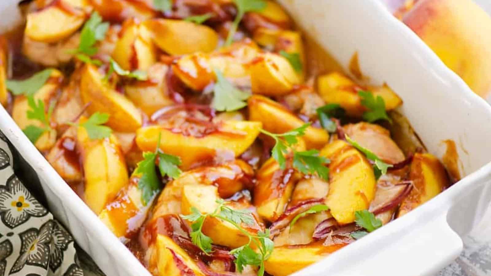 Baked chicken with sliced peaches, red onions, barbecue sauce, and fresh parsley in a white baking dish.