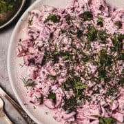 Diced beet salad with creamy dressing, topped with fresh herbs, served on a white plate.