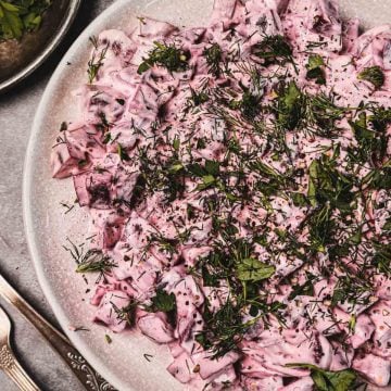 Diced beet salad with creamy dressing, topped with fresh herbs, served on a white plate.