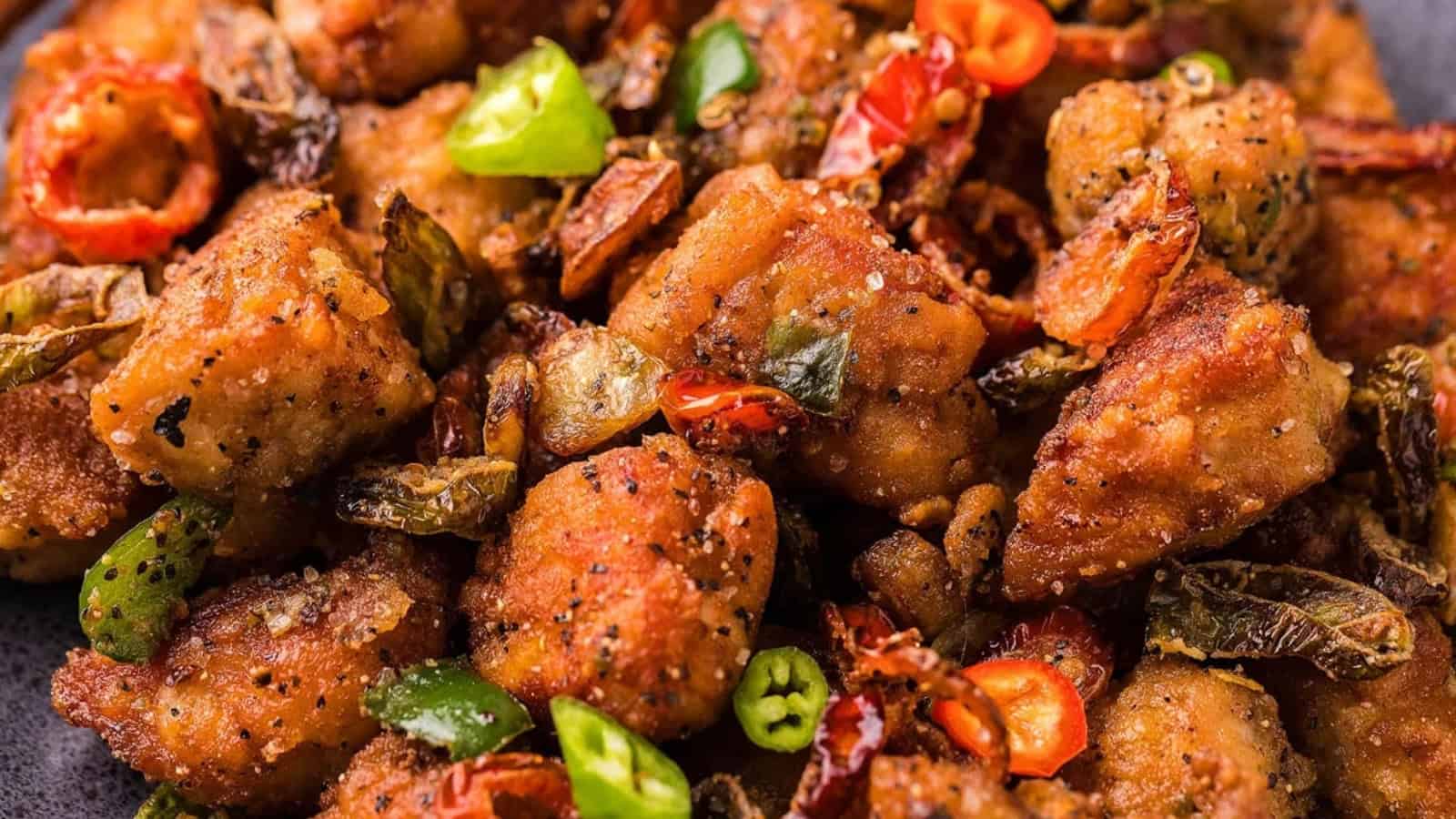Close-up of crispy fried chicken pieces garnished with sliced green and red chilies and herbs.