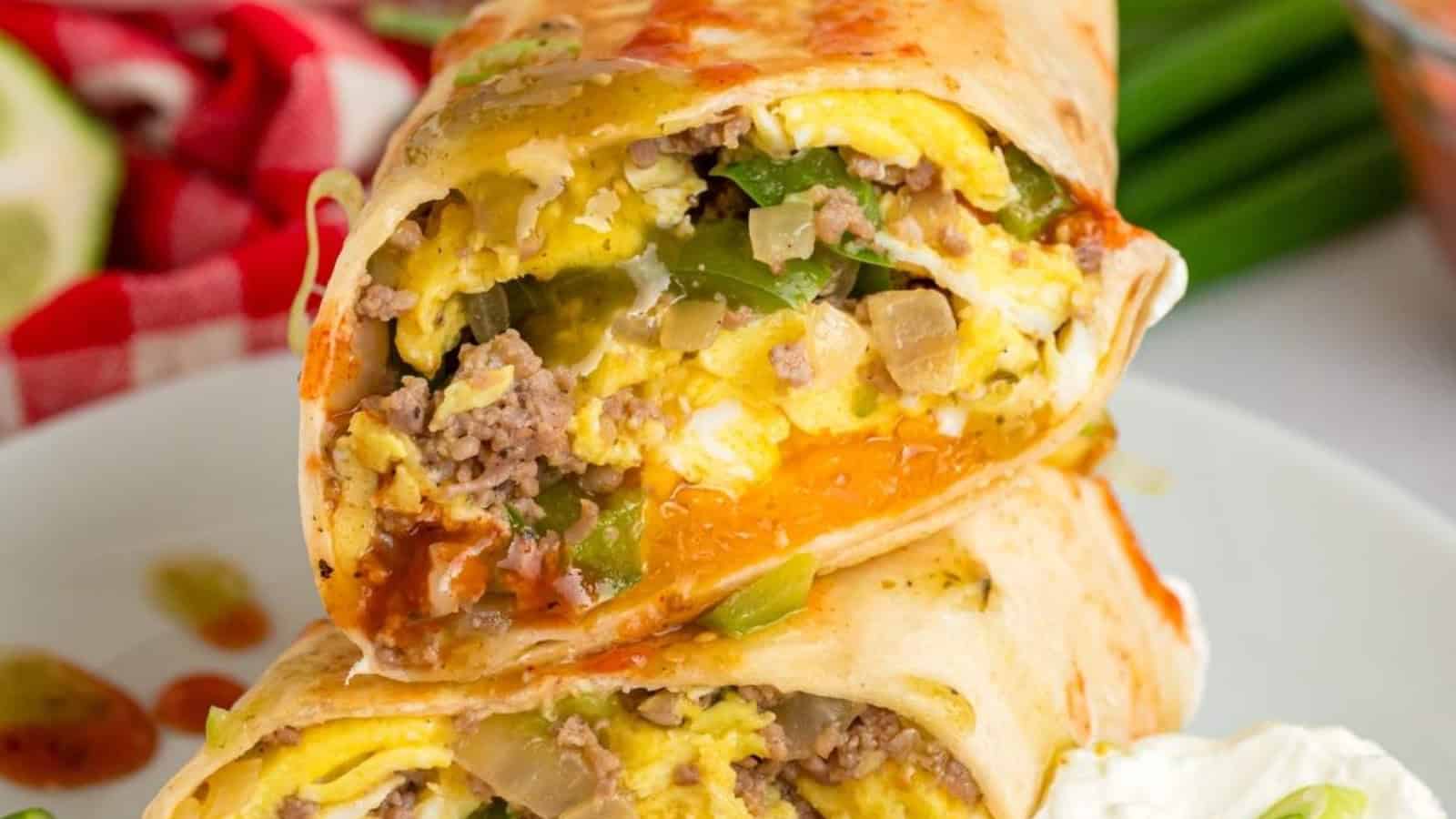 A breakfast burrito cut in half, filled with eggs, sausage, peppers, and cheese, served with sour cream.