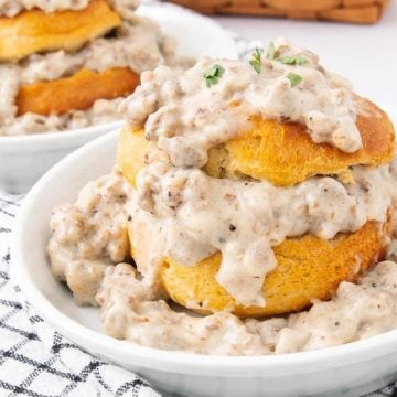 Biscuits topped with creamy sausage gravy served in white bowls on a checkered cloth.