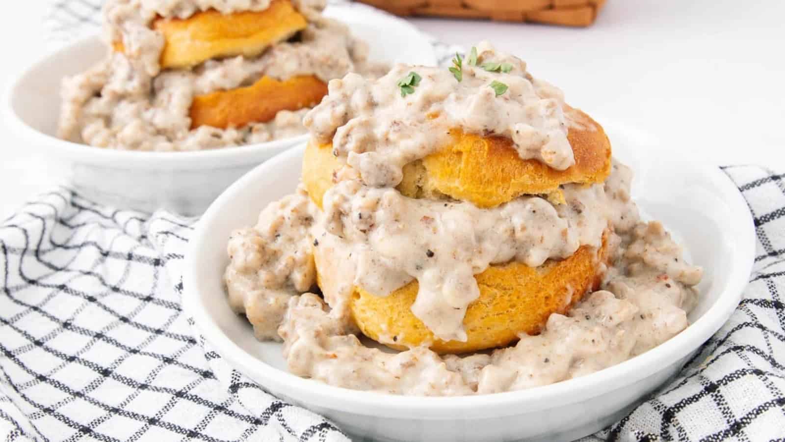 Biscuits topped with creamy sausage gravy served in white bowls on a checkered cloth.