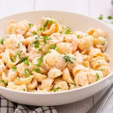 A bowl of creamy shell pasta garnished with chopped parsley, next to silverware on a striped napkin.