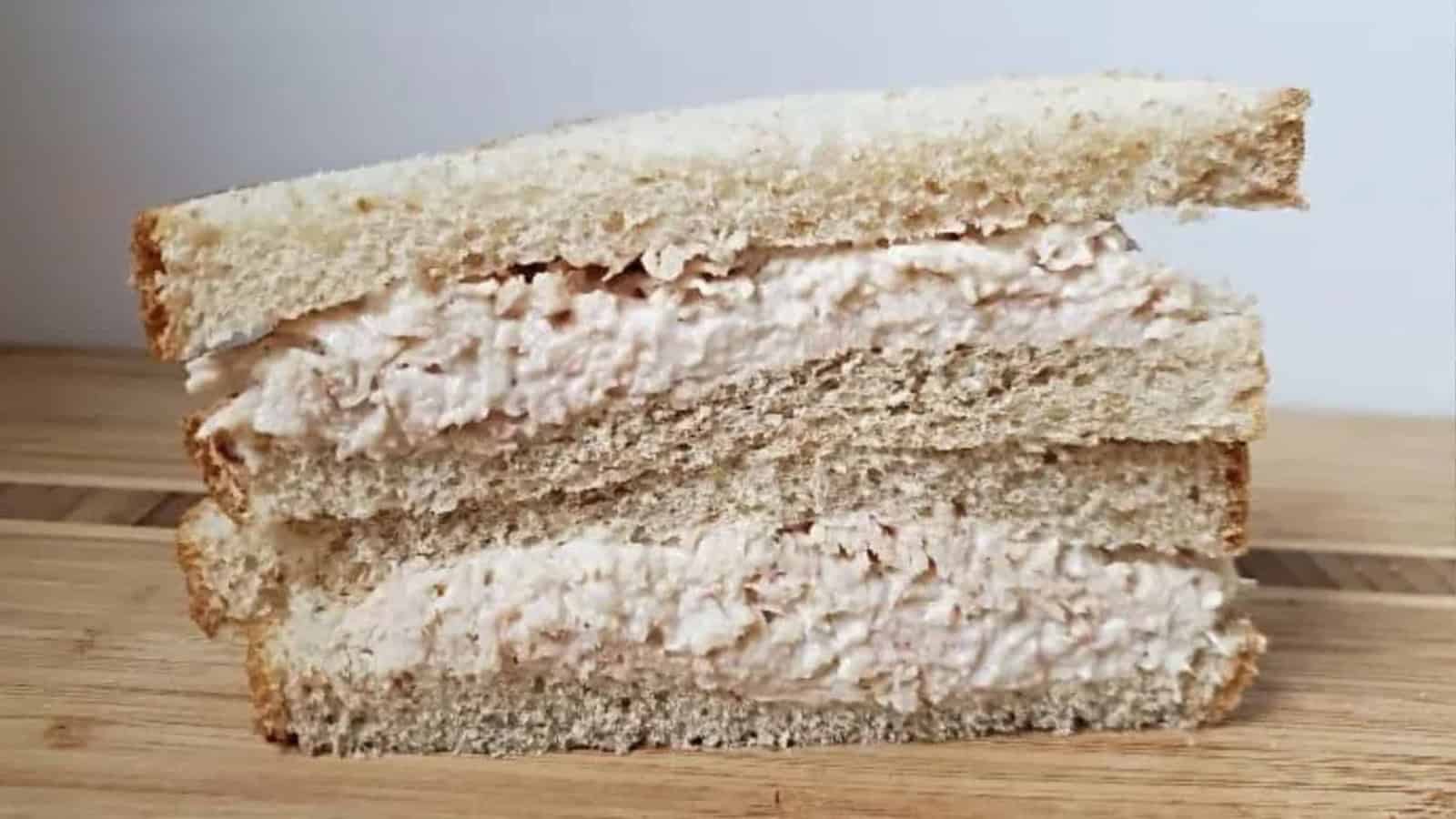 Image shows a Canned Chicken Salad sandwich on a wooden table.