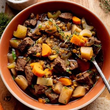 A bowl of hearty beef and vegetable stew with carrots, turnips, and lentils on a rustic table.