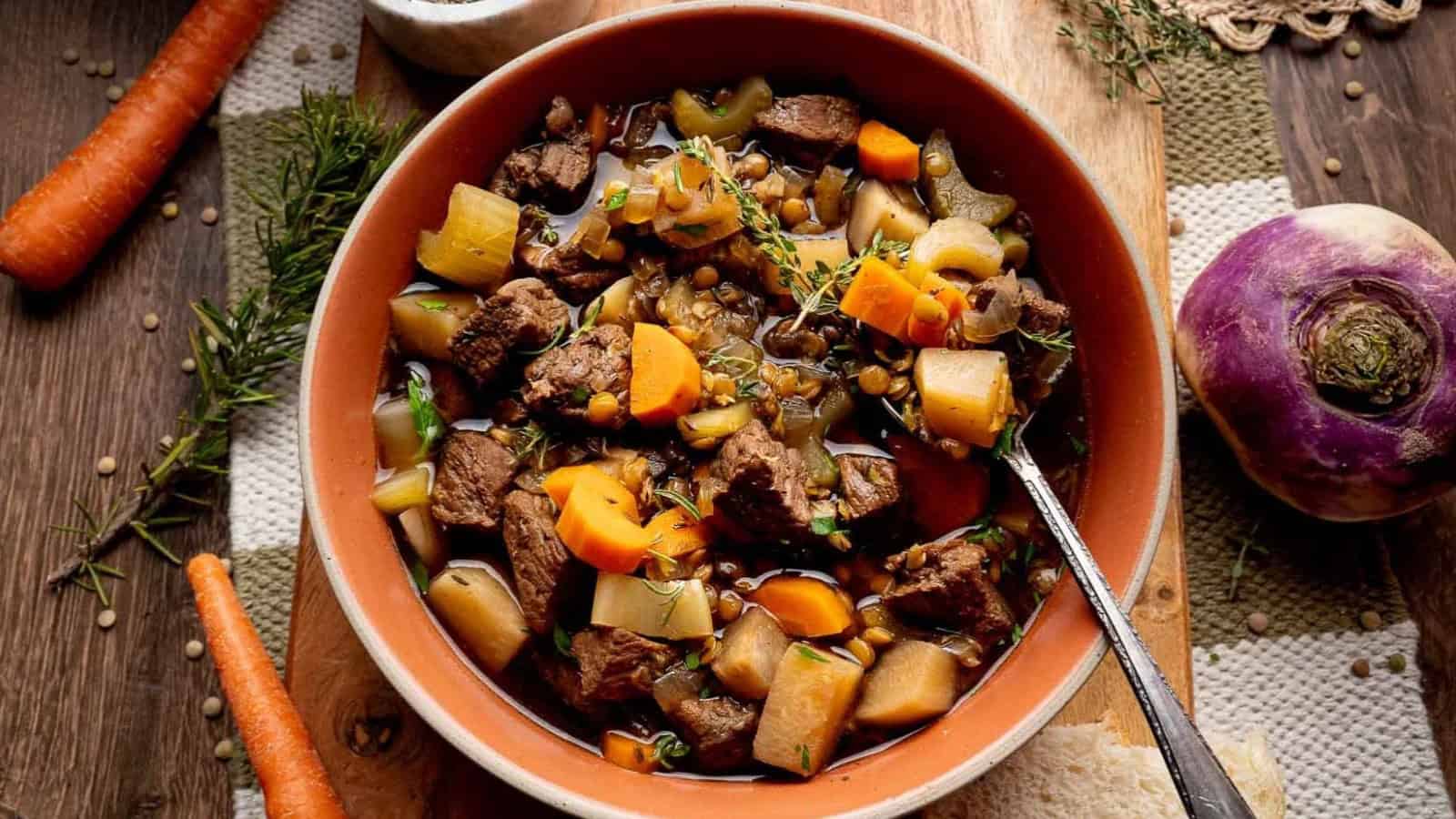 A bowl of hearty beef and vegetable stew with carrots, turnips, and lentils on a rustic table.