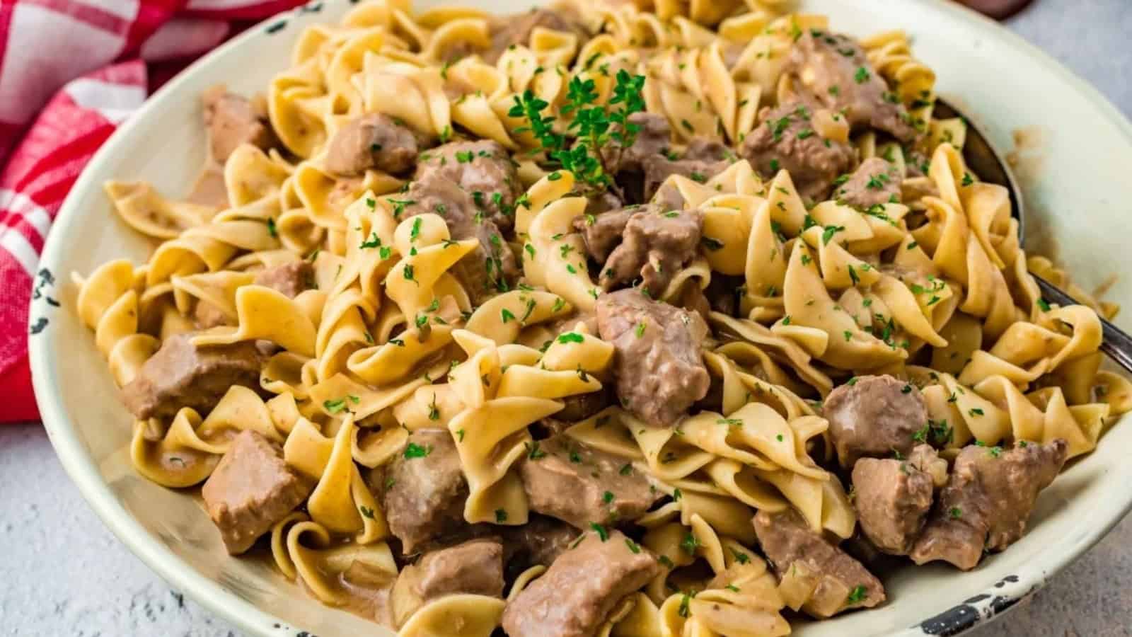 A plate of beef stroganoff with egg noodles, creamy sauce, and garnished with chopped parsley.