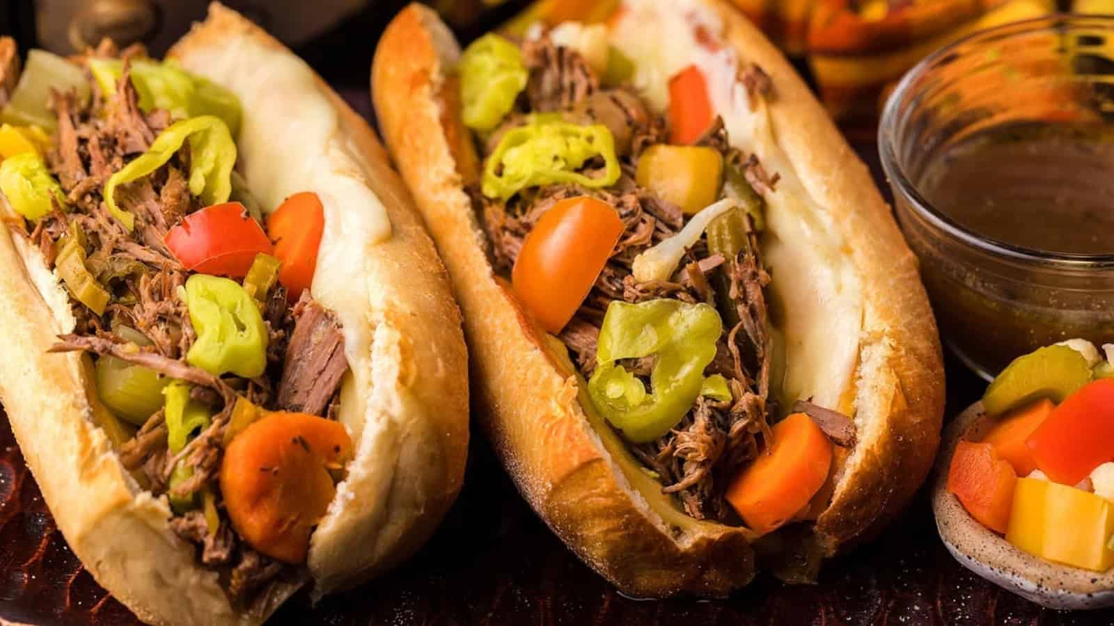 Two Italian beef sandwiches with shredded meat, peppers, tomatoes, and melted cheese on hoagie rolls.