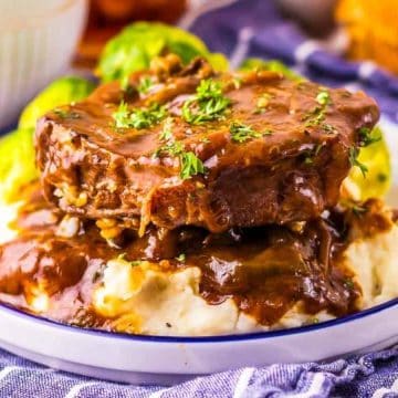 Two pieces of Salisbury steak with gravy on mashed potatoes, garnished with parsley on a white plate.