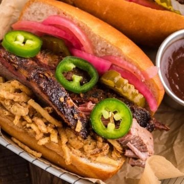 Two barbecue brisket sandwiches with pickled onions, jalapeños, and crispy onions, served with barbecue sauce.