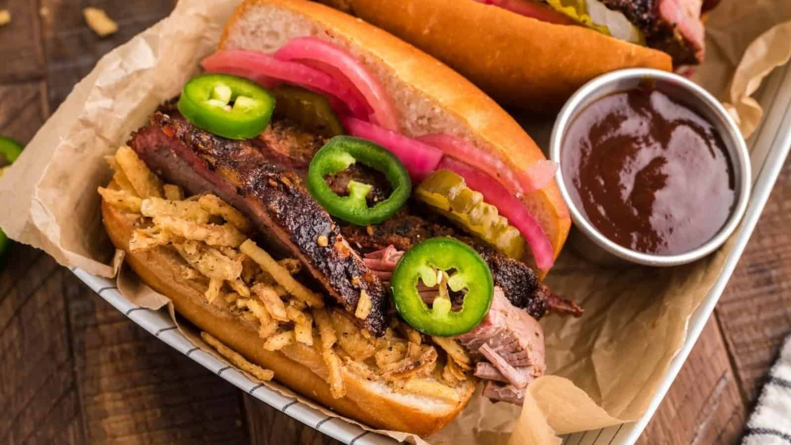 Two barbecue brisket sandwiches with pickled onions, jalape&ntilde;os, and crispy onions, served with barbecue sauce.