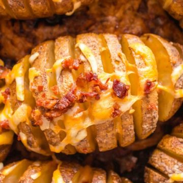 Hasselback potatoes topped with melted cheese and crispy bacon pieces.