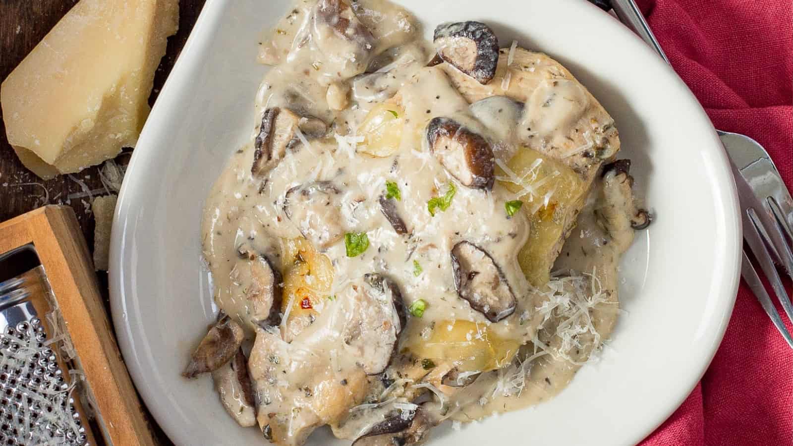 Pasta with creamy mushroom sauce, grated cheese, and herbs, served on a white plate with a fork and cheese wedge.