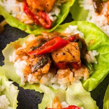 Lettuce wraps filled with rice, chicken, red peppers, and vegetables on a dark surface.