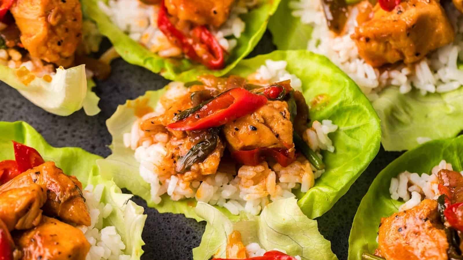 Lettuce wraps filled with rice, chicken, red peppers, and vegetables on a dark surface.