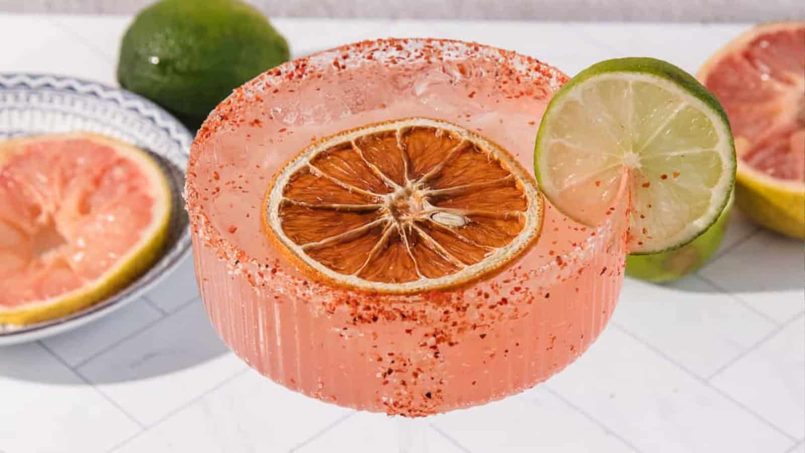 A pink cocktail in a ribbed glass with chili rim, dried grapefruit, and lime garnish.