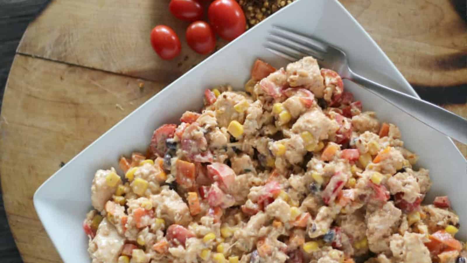 Plate of chicken salad next to spices and tomatoes.