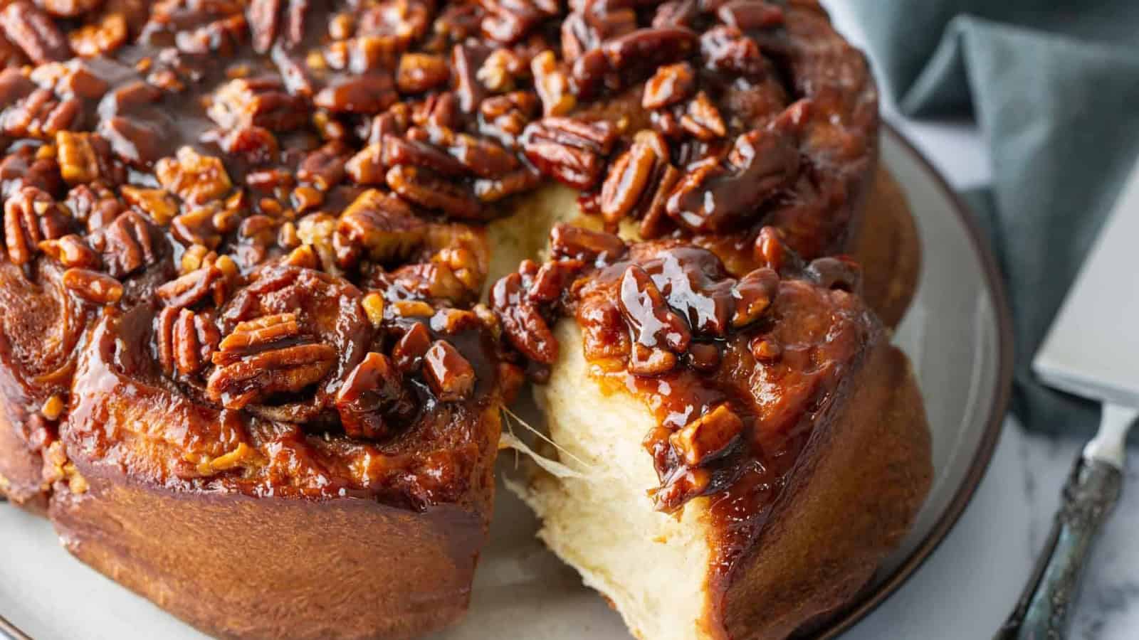 Sticky pecan-topped sweet rolls with a gooey caramel glaze, one roll has been pulled away from the rest.