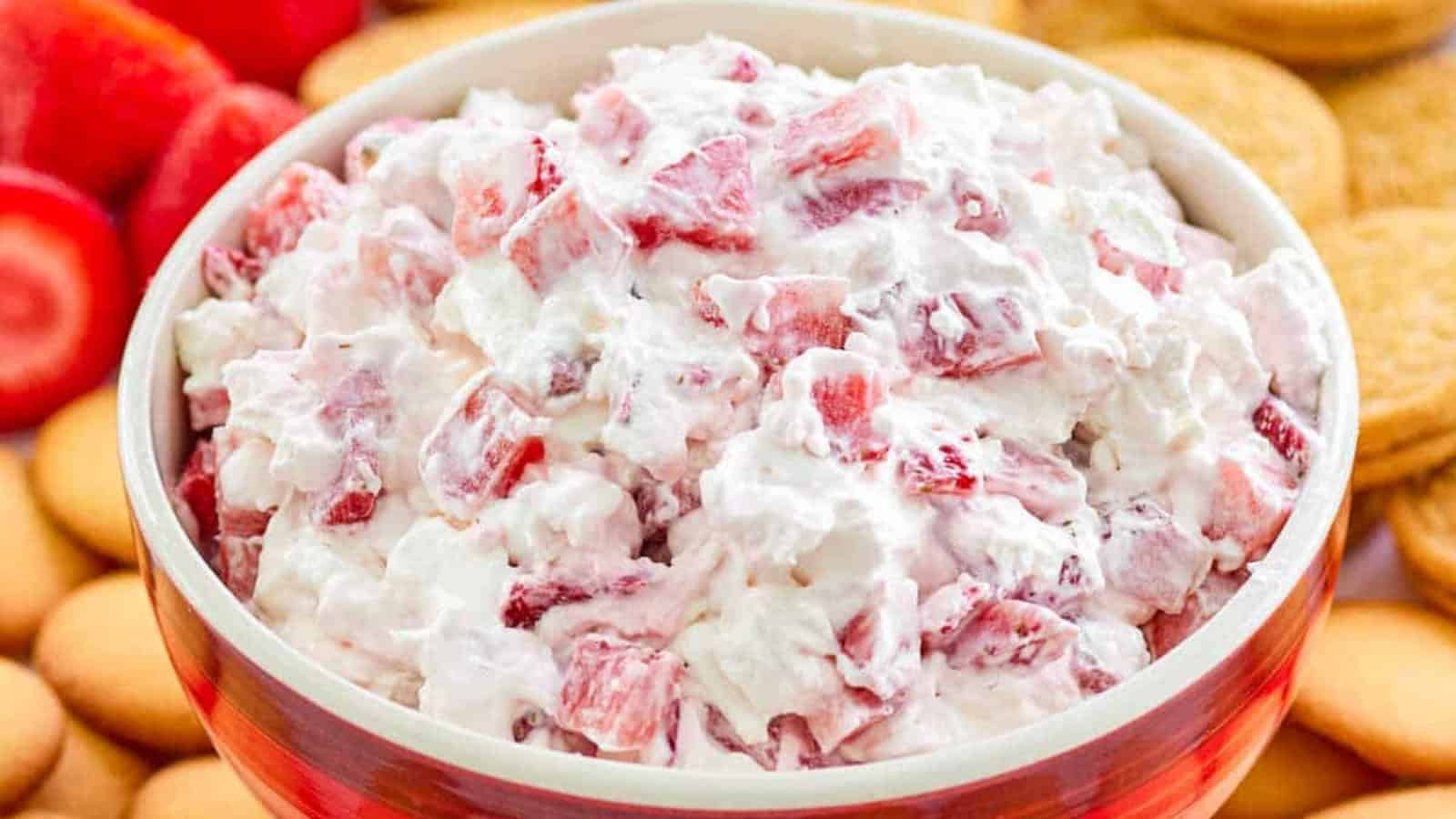 A bowl of creamy strawberry dessert salad with cookie and strawberry slices in the background.