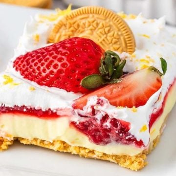 A slice of layered dessert with cream, strawberries, a cookie, and a golden crust on a white plate.
