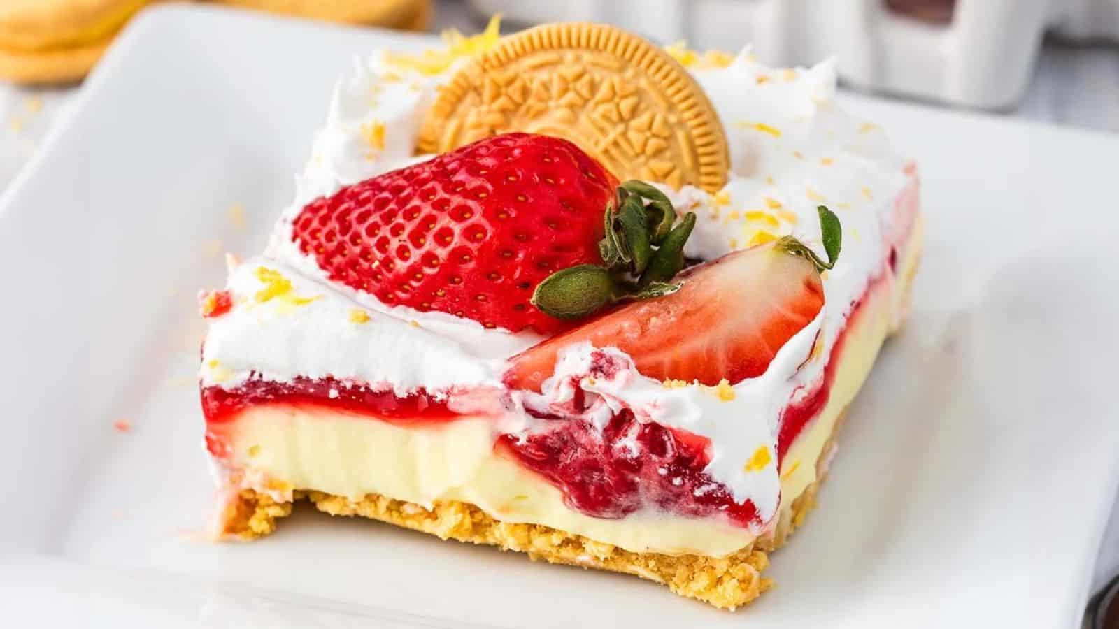 A slice of layered dessert with cream, strawberries, a cookie, and a golden crust on a white plate.