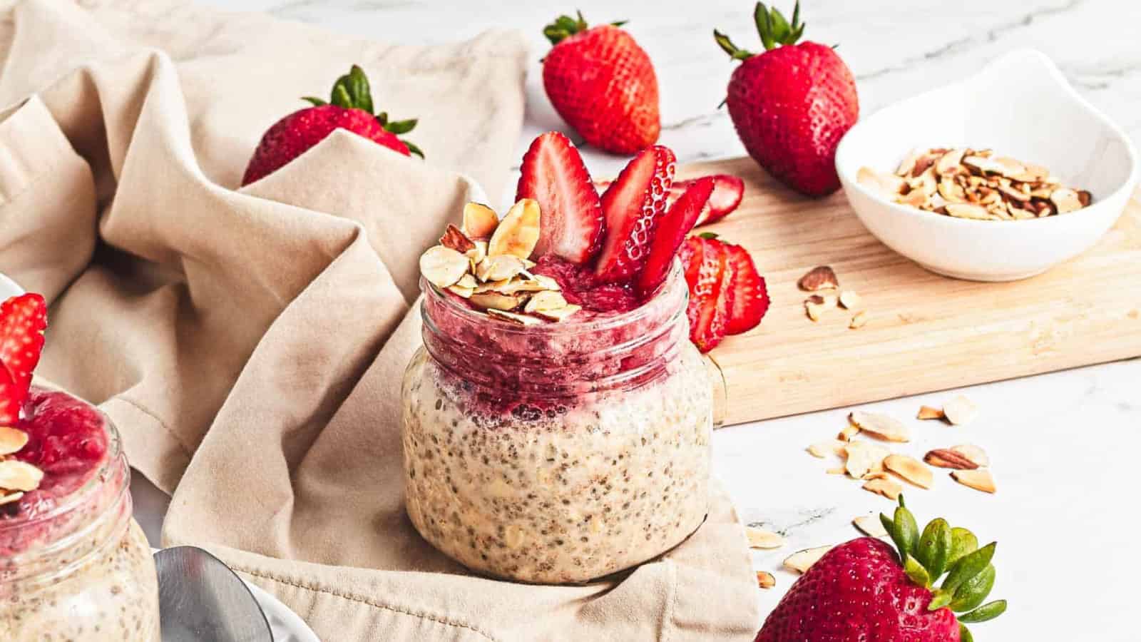 A jar of chia pudding topped with sliced strawberries and almonds, surrounded by fresh strawberries.
