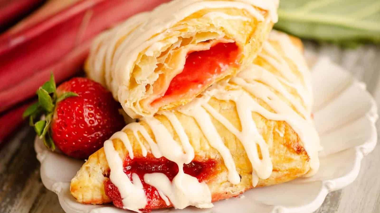 Two flaky pastries with strawberry filling and white icing, stacked on a plate with fresh strawberries.