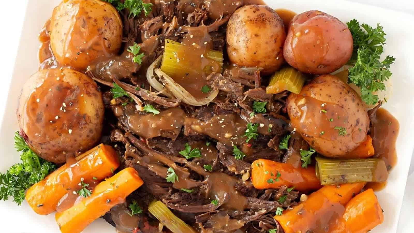Pot roast with gravy, potatoes, carrots, celery, and parsley served on a white plate.