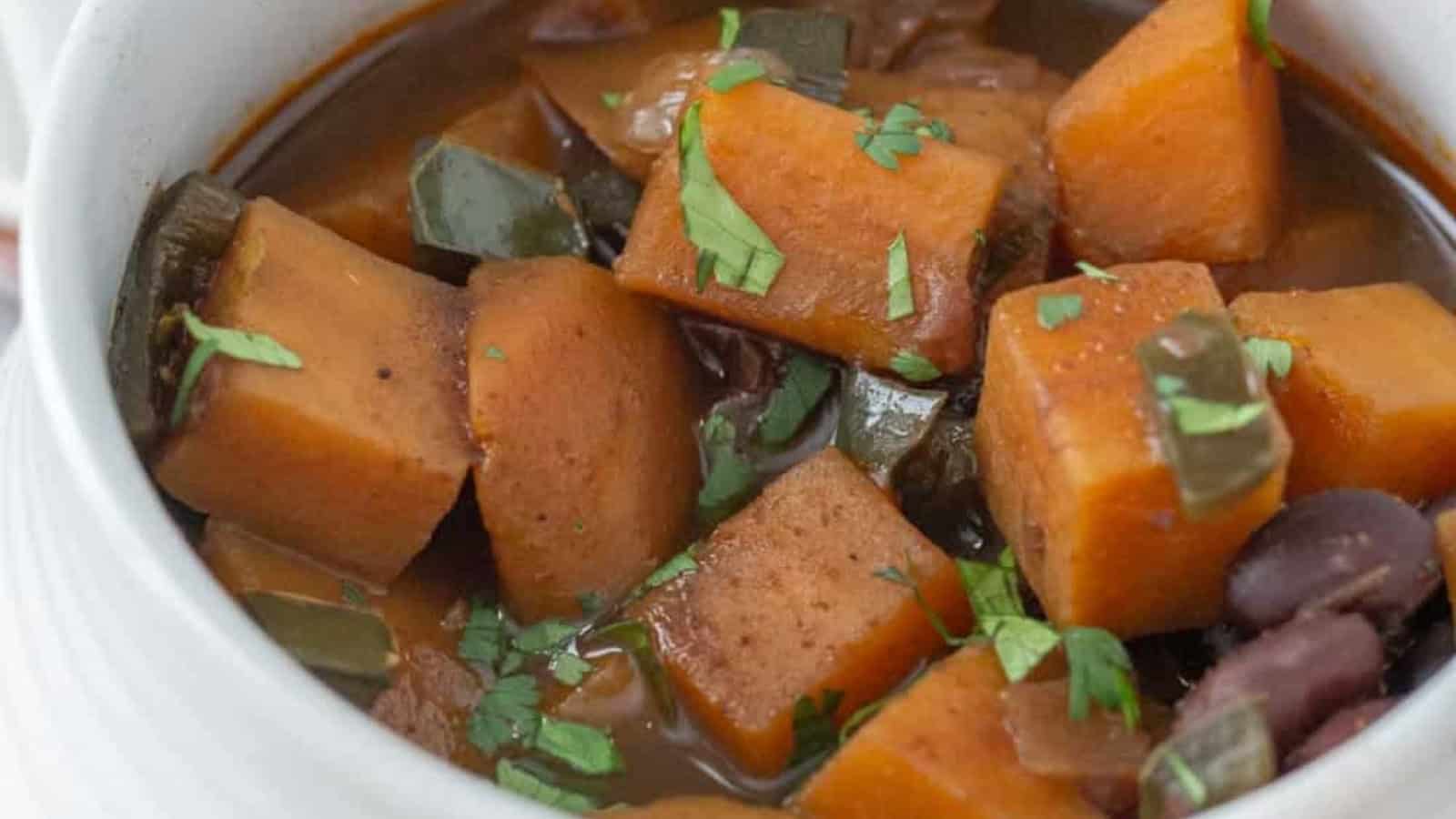 Close-up of a bowl of stew with sweet potatoes, green peppers, kidney beans, and chopped cilantro on top.