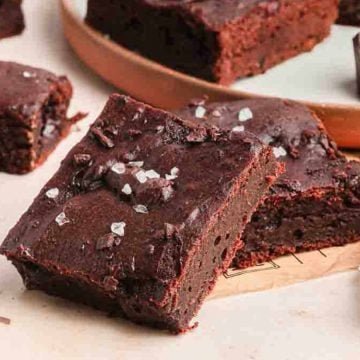 Fudgy chocolate brownies topped with sea salt flakes, with chunks of chocolate on a light surface.