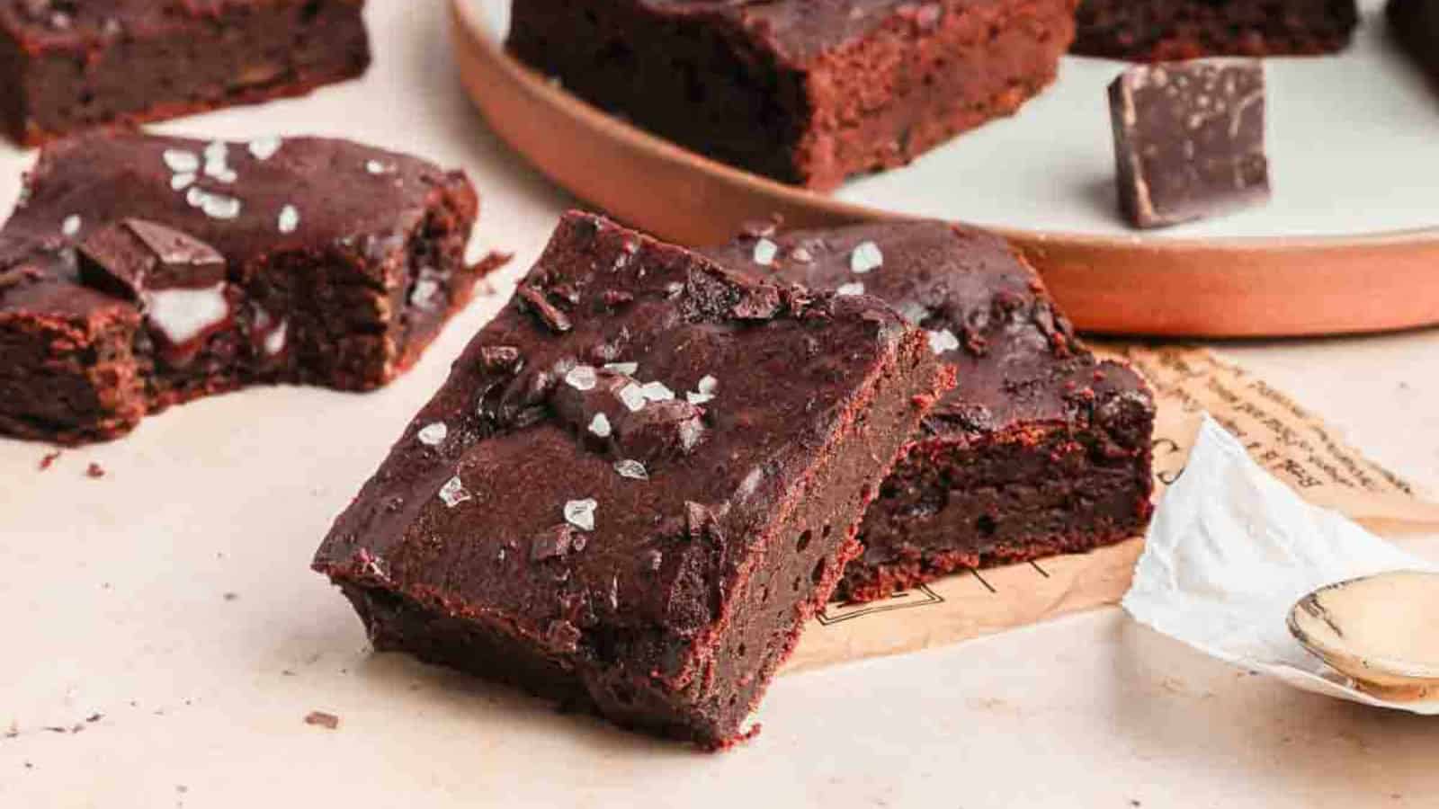 Fudgy chocolate brownies topped with sea salt flakes, with chunks of chocolate on a light surface.