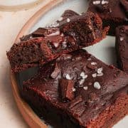 Close-up of fudgy chocolate brownies topped with sea salt flakes and chocolate chunks on a plate.
