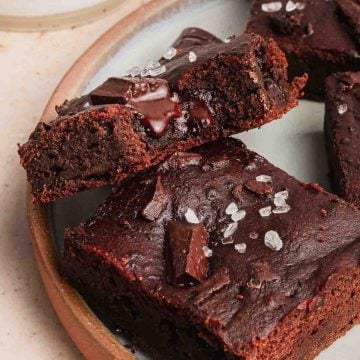 Close-up of fudgy chocolate brownies topped with sea salt flakes and chocolate chunks on a plate.