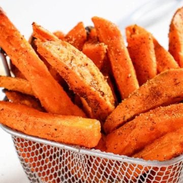 Seasoned sweet potato fries in a metal basket, with a bowl of ketchup in the background.