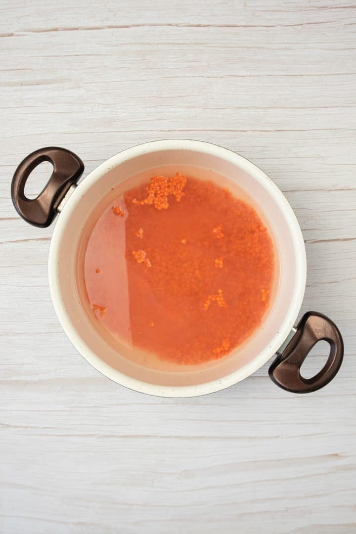 A white pot with handles contains red lentils soaking in water on a light wooden surface-perfect for making sweet potato and red lentil burgers.
