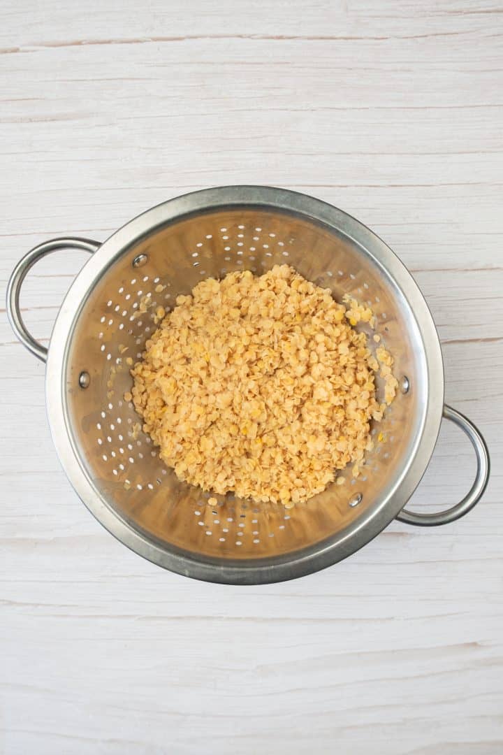 Cooked red lentils, perfect for sweet potato and red lentil burgers, draining in a metal colander on a light wood surface.