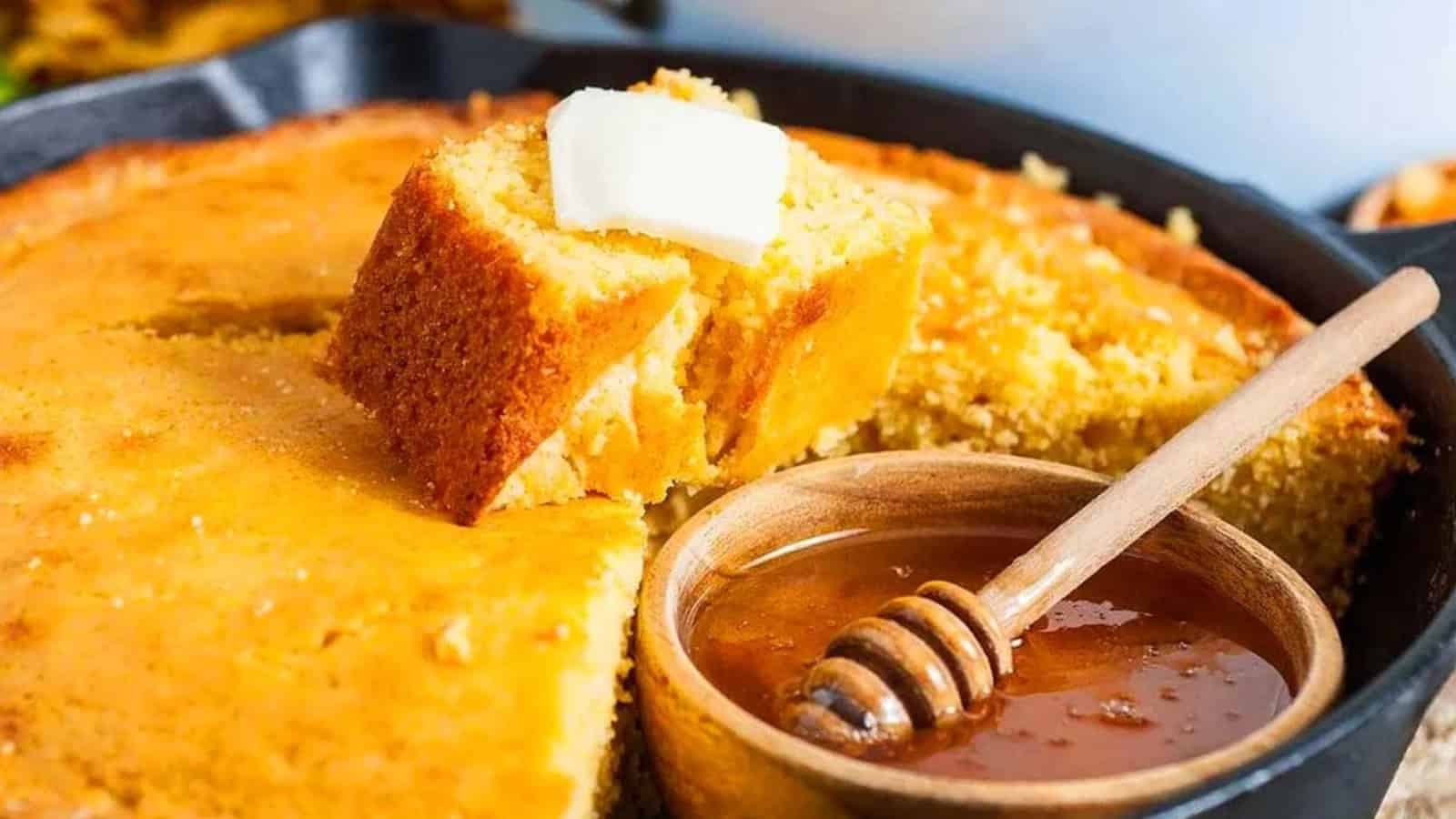 A slice of cornbread with butter sits on top, next to a bowl of honey with a dipper.