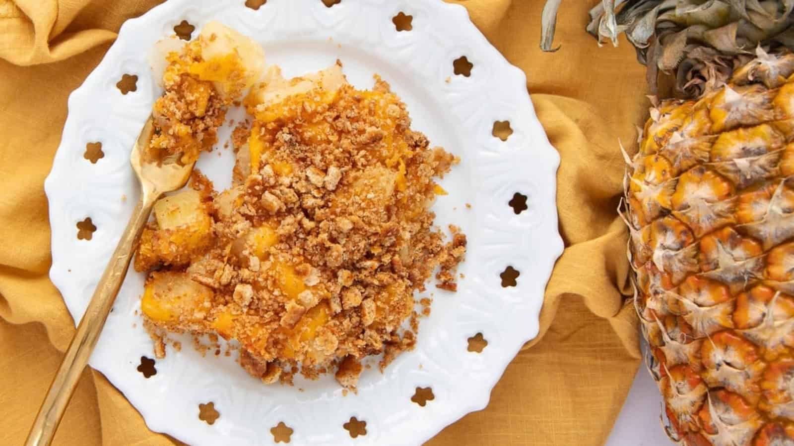 A plate of pineapple crumble on a white dish with a fork, next to a fresh pineapple and a yellow napkin.