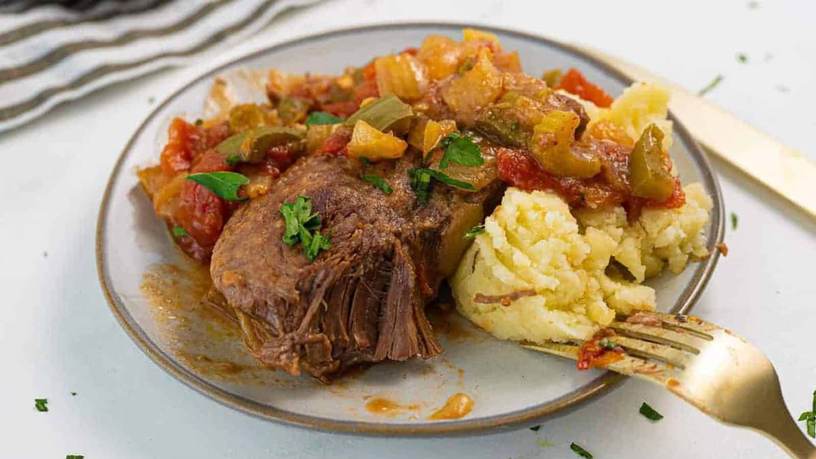 Plate with mashed potatoes and pot roast topped with tomato and vegetable gravy, garnished with parsley.
